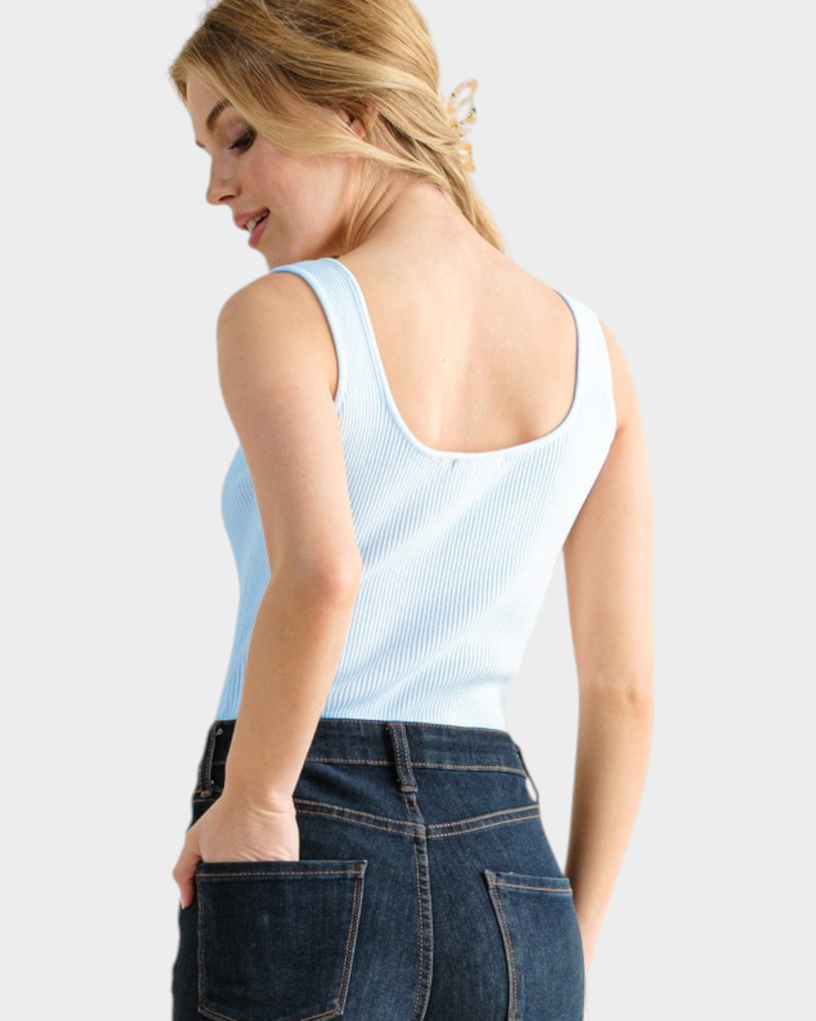 Woman wearing a light blue tank top and dark blue jeans against a white background