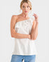 Woman wearing a white one-shoulder top and blue jeans on a light gray background