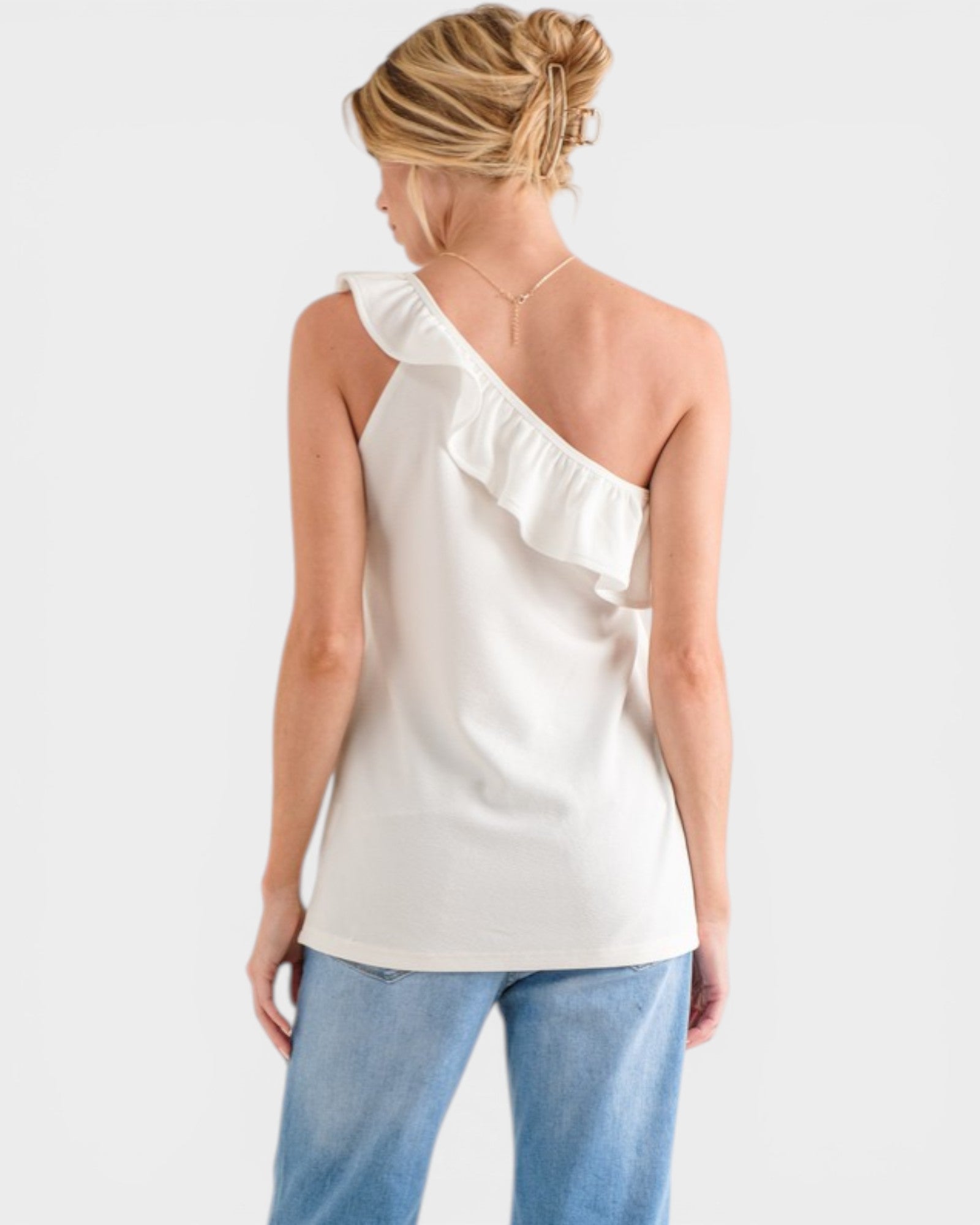 Woman wearing a white one-shoulder top and blue jeans on a white background