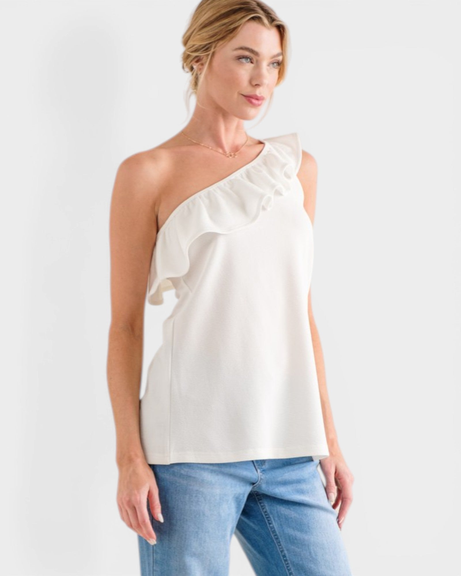 Woman wearing a white one-shoulder top and blue jeans on a white background