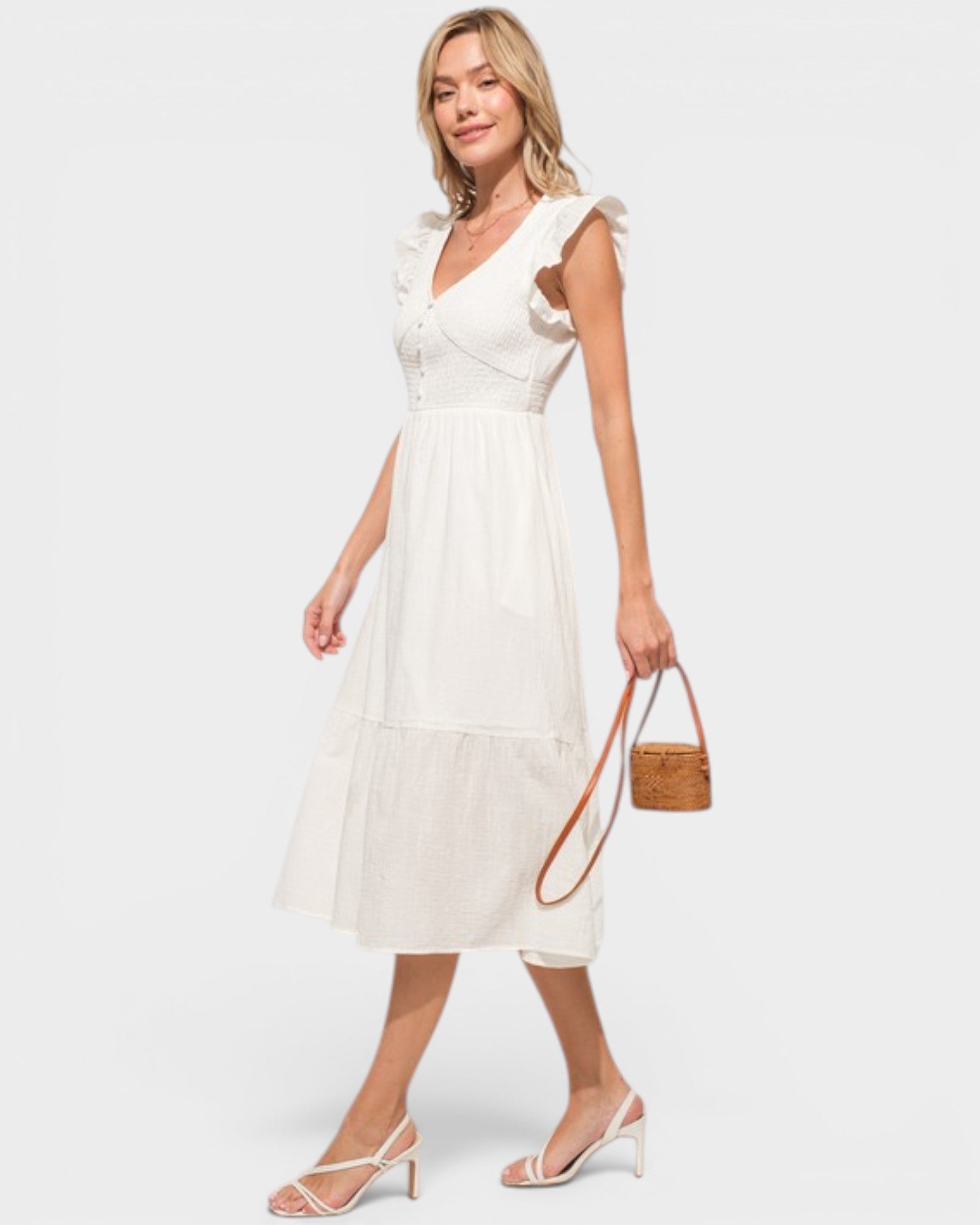 Woman wearing a white dress holding a woven handbag on a plain background
