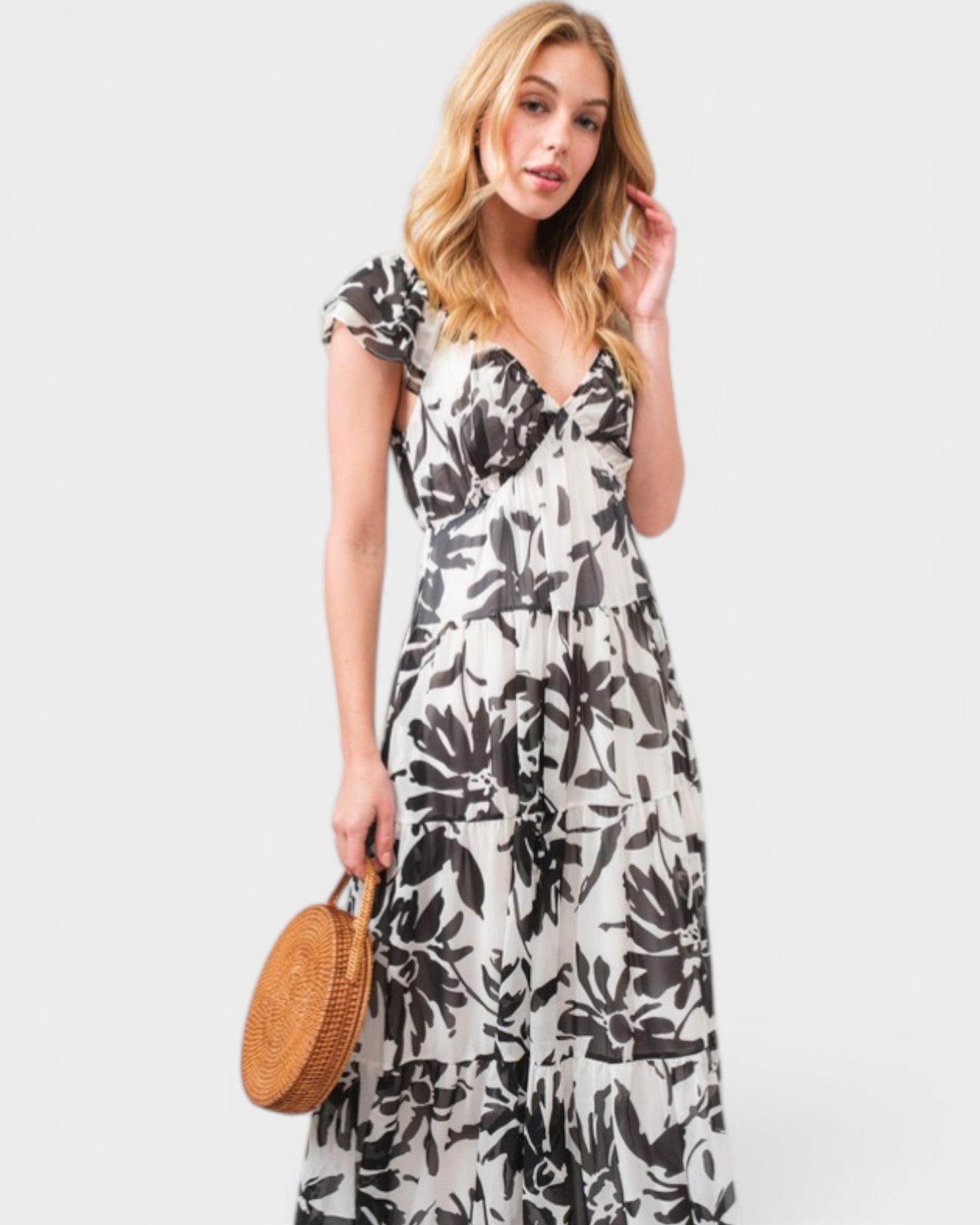 Woman wearing a floral dress holding a round woven bag on a white background