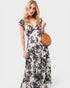 Woman wearing a black and white floral dress holding a round brown bag on a white background