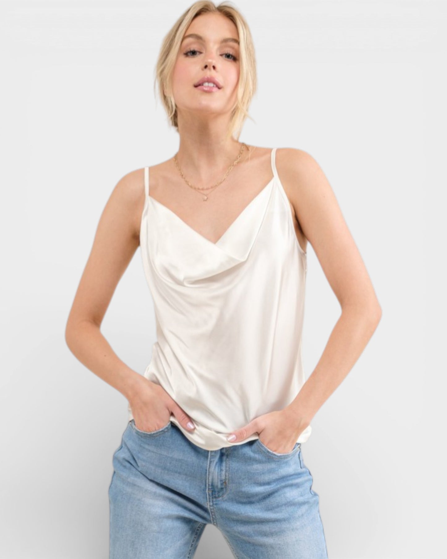 Woman wearing a cream-colored tank top and light blue jeans on a white background