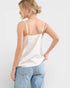 Woman wearing a white satin camisole and light blue jeans on a plain background