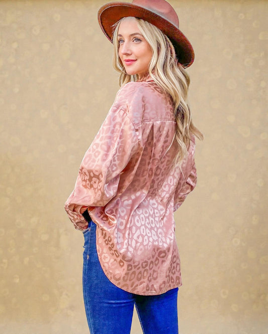 Woman wearing a pink leopard print blouse and blue jeans with a brown hat against a beige background