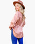 A woman wearing a pink leopard-print long-sleeve blouse, blue jeans, and a brown wide-brim hat, photographed against a plain light gray studio background.