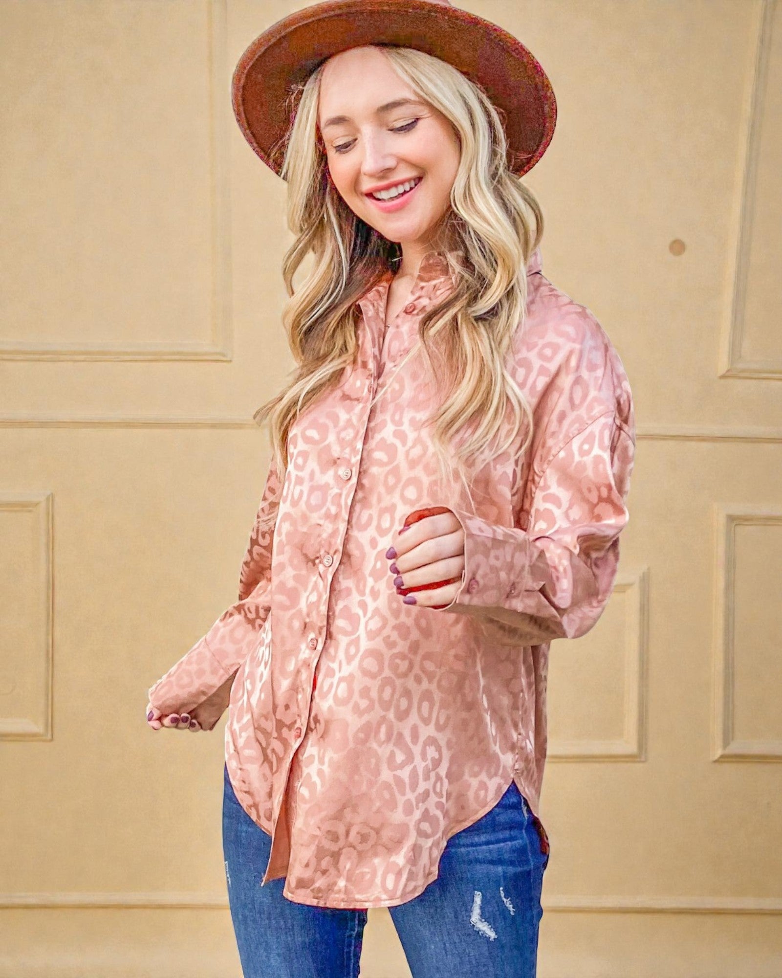 Woman wearing a pink leopard print shirt and blue jeans with a beige background