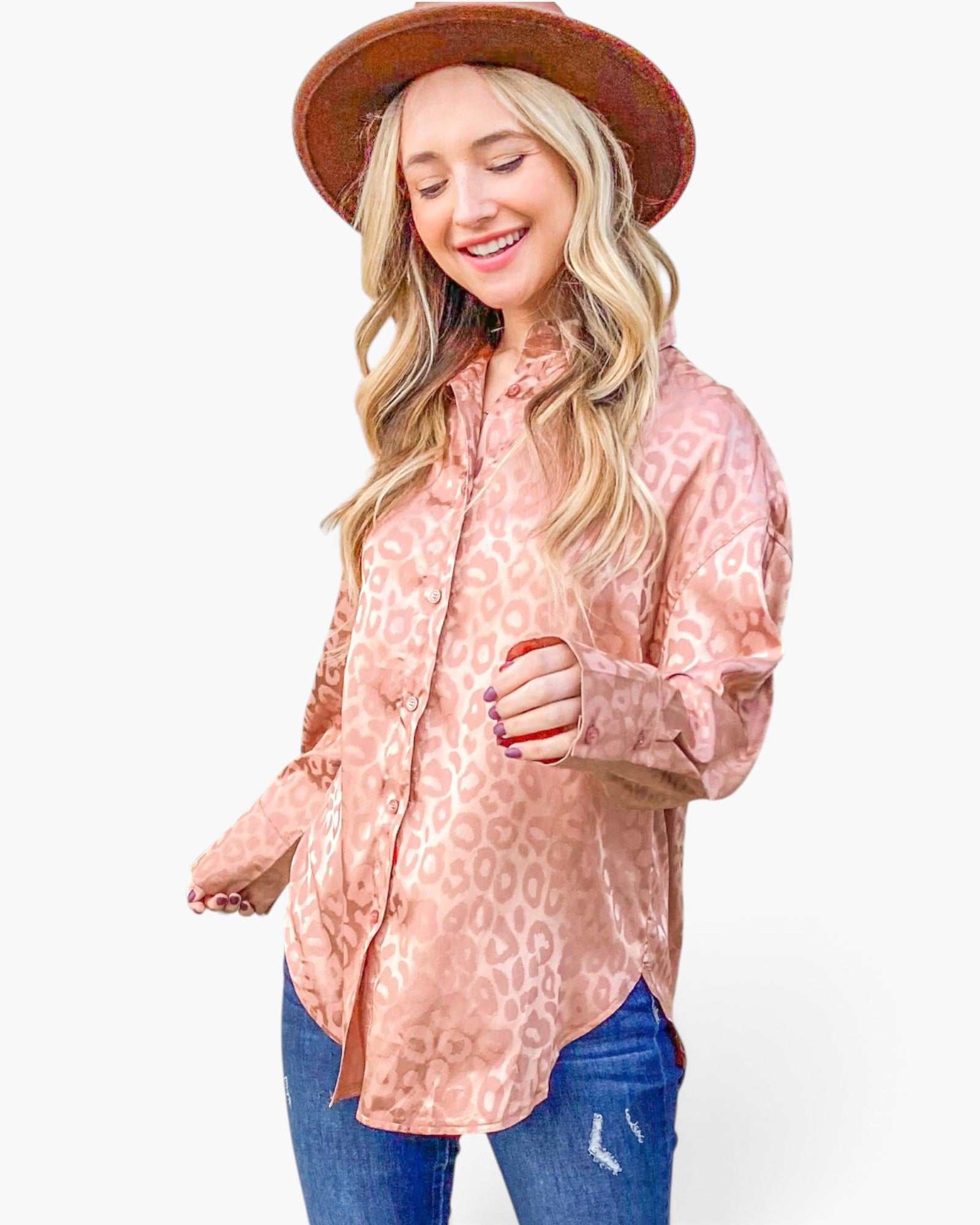 A woman wearing a dusty pink leopard-print button-up shirt, blue jeans, and a brown wide-brim hat, photographed against a solid white background.