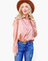 A woman modeling a long-sleeve button-up shirt with a pink and beige leopard print, paired with blue jeans, a black belt with a gold buckle, and a brown hat, against a plain white background.