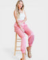 Woman wearing pink pants sitting on a wooden stool against a white background
