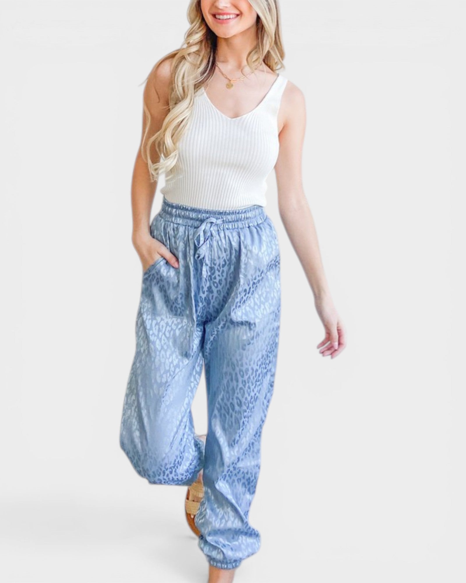 Woman wearing a white sleeveless top and blue patterned pants on a white background