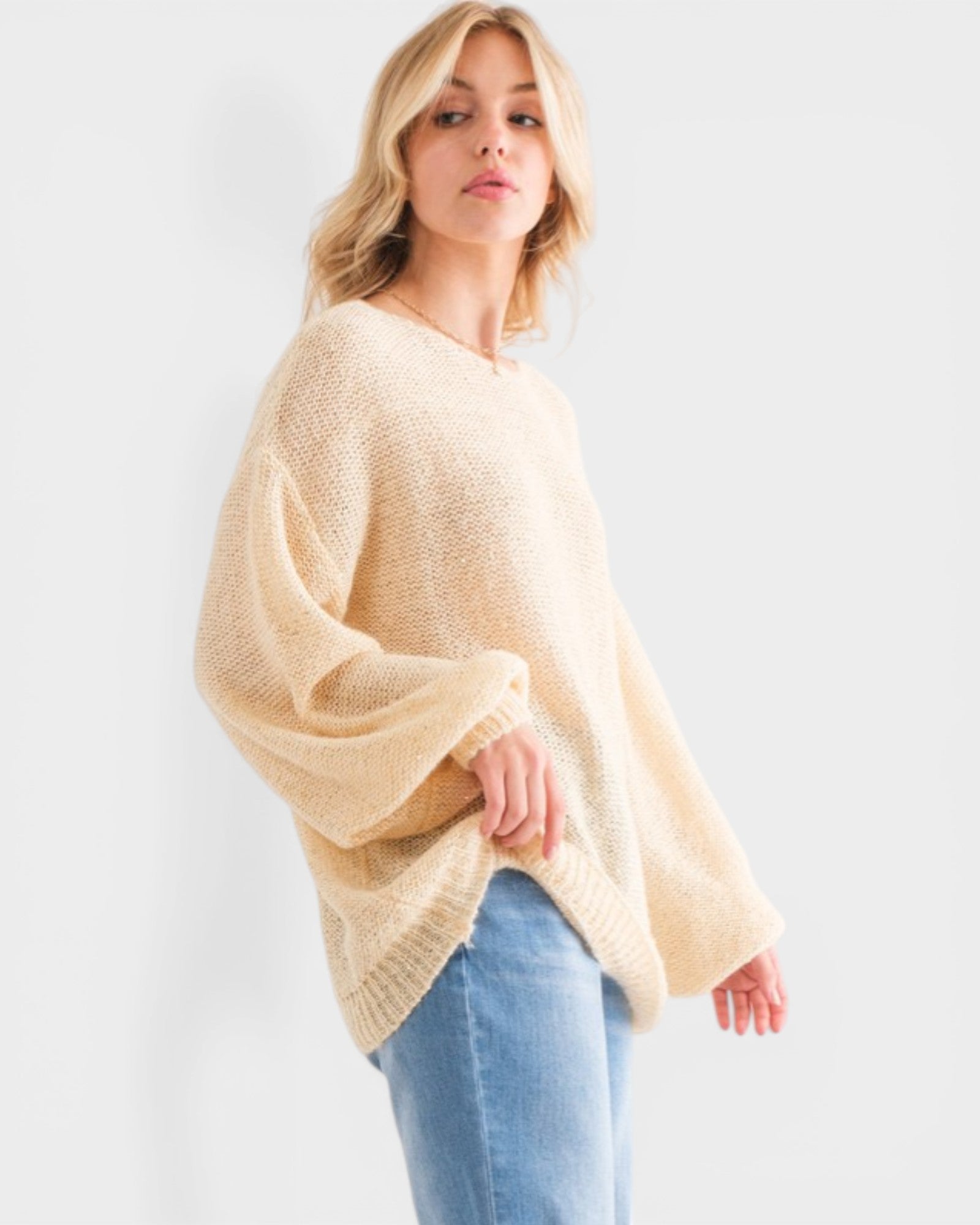 Woman wearing a beige sweater and blue jeans against a white background