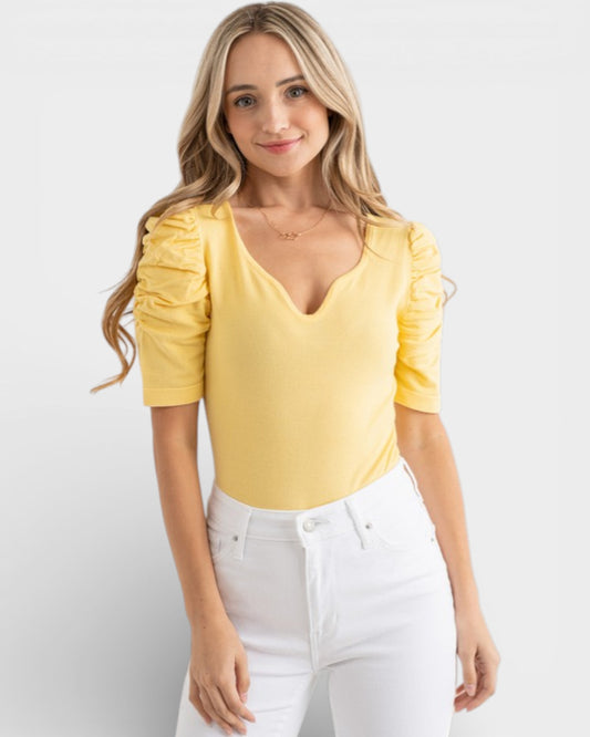Woman wearing a yellow top with puff sleeves against a white background