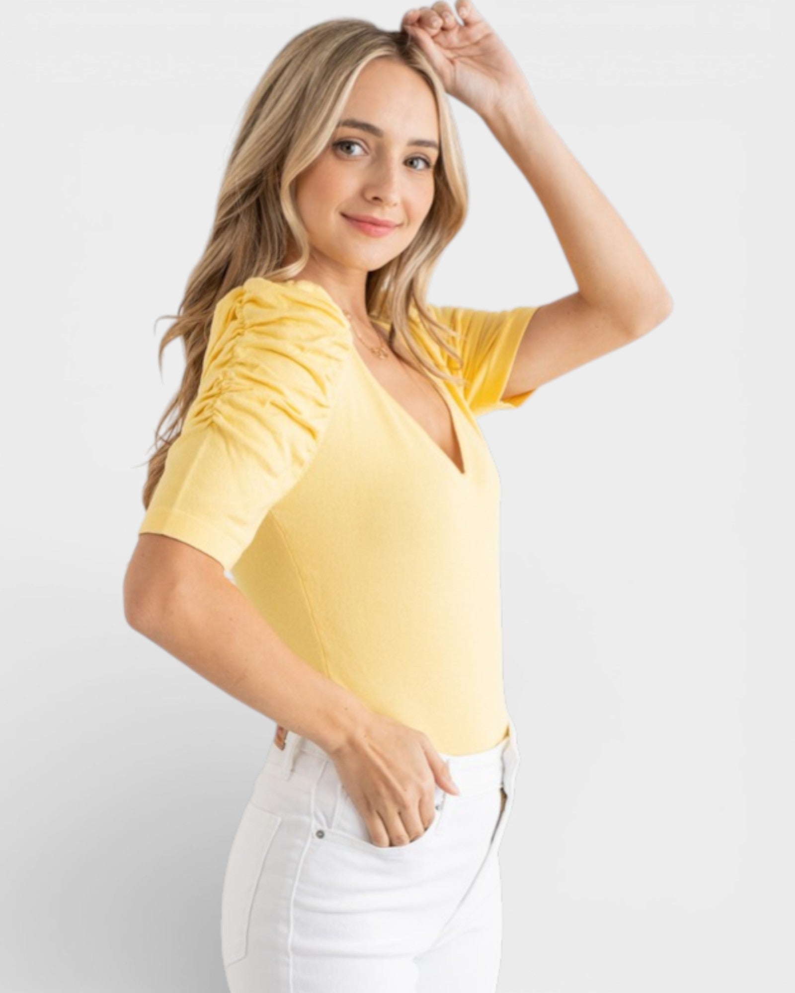 Woman wearing a yellow top and white pants against a plain background