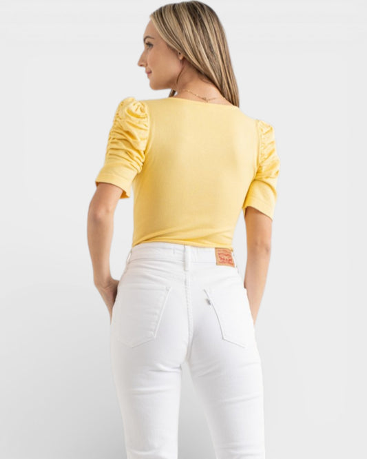 Woman wearing a yellow top and white pants on a light gray background