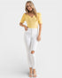 Woman wearing a yellow top and white pants on a light gray background