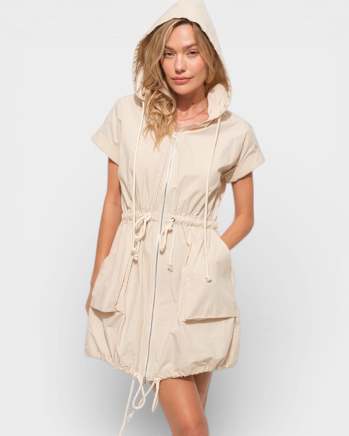 Woman wearing a beige hooded dress against a white background