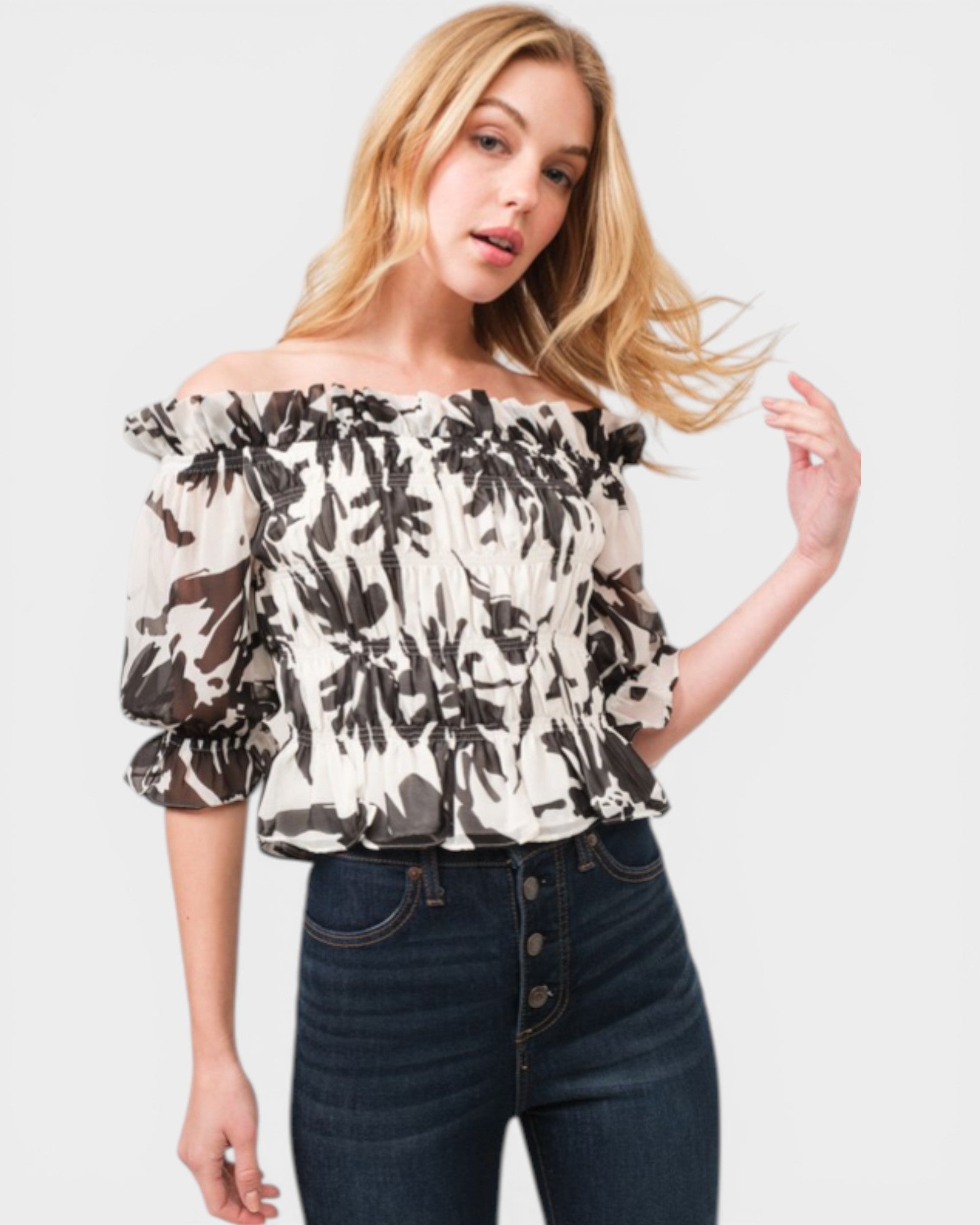 Woman wearing a floral off-shoulder top and jeans on a plain background