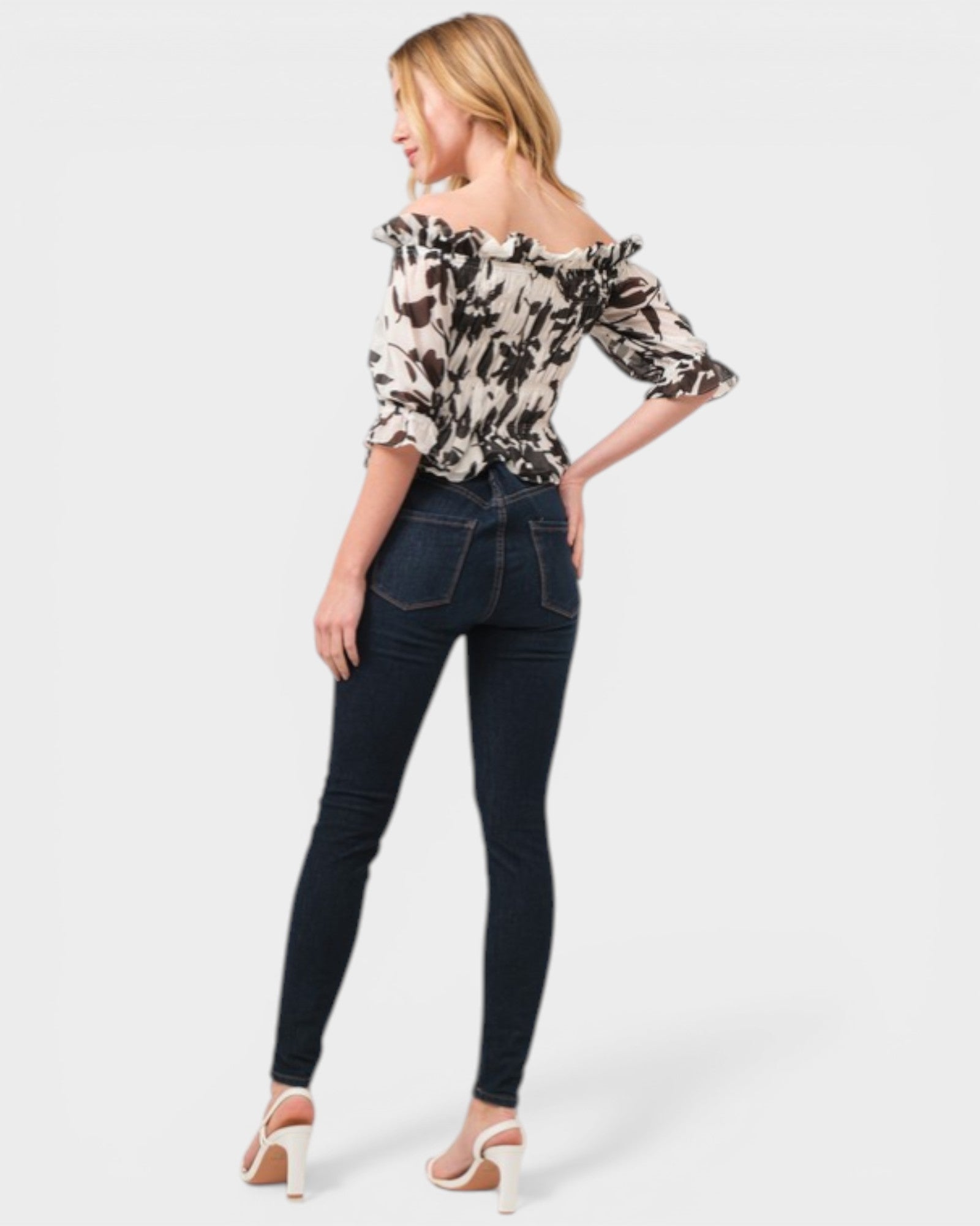 Woman wearing a floral blouse and dark jeans on a white background