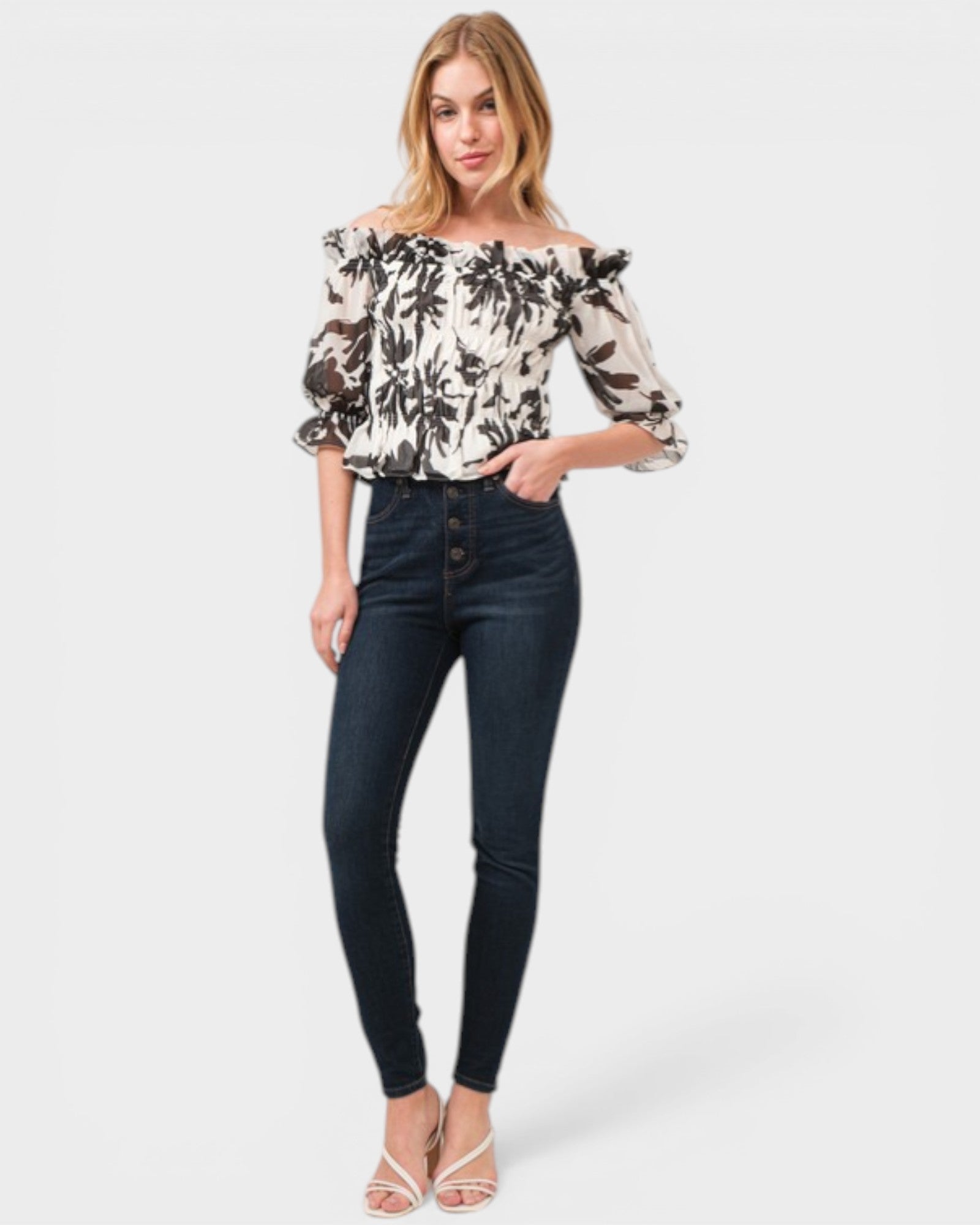 Woman wearing a floral off-shoulder top and dark jeans on a white background