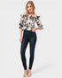 Woman wearing a floral off-shoulder top and dark jeans on a white background