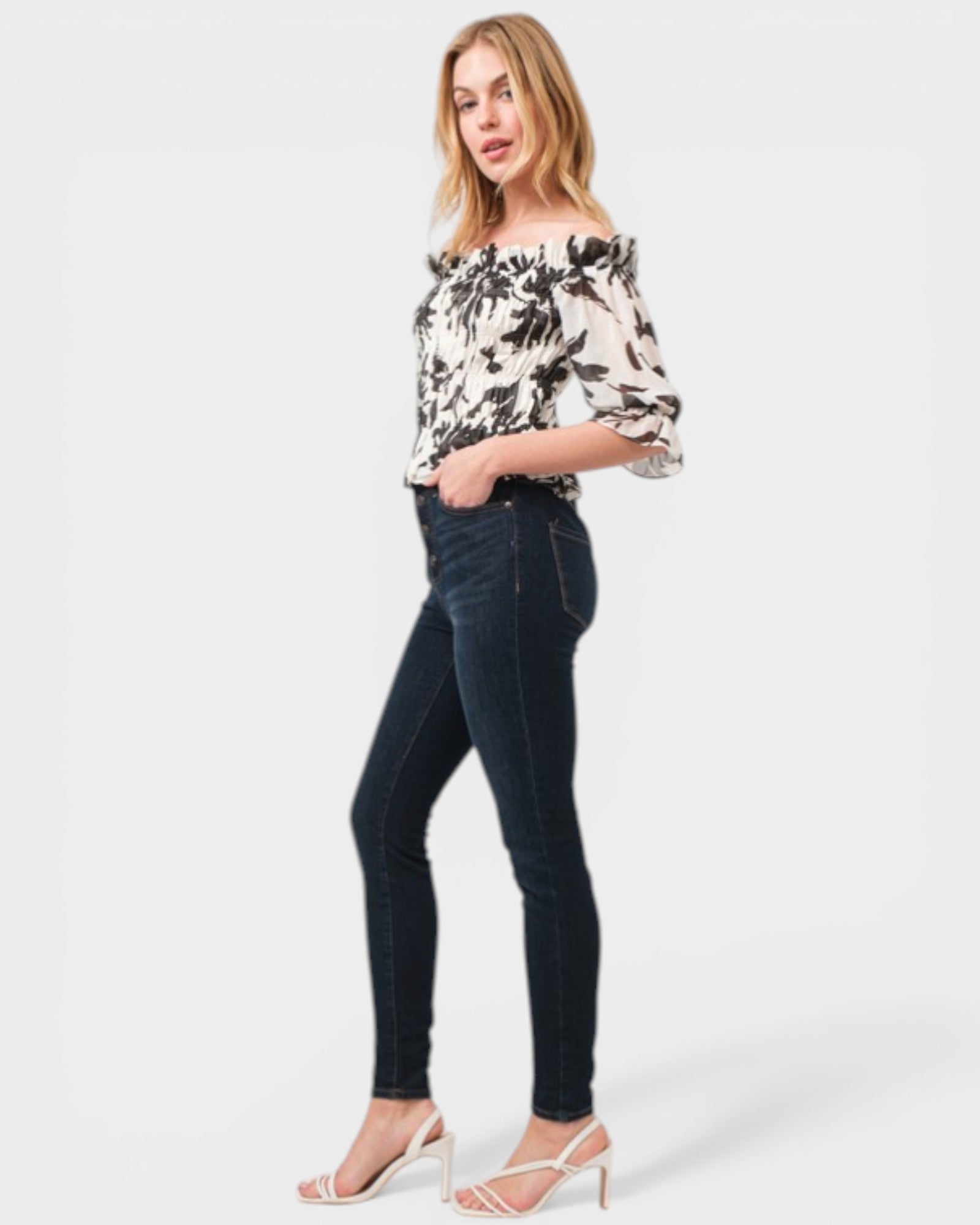 Woman wearing a floral off-shoulder top and dark jeans on a white background