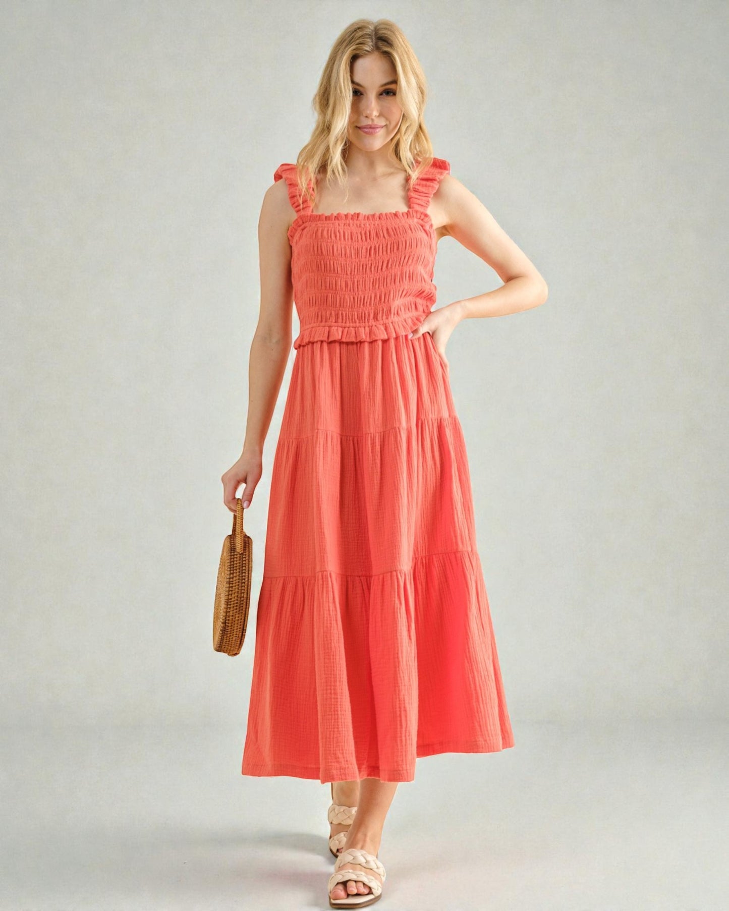 Woman wearing a coral dress holding a woven bag on a plain background