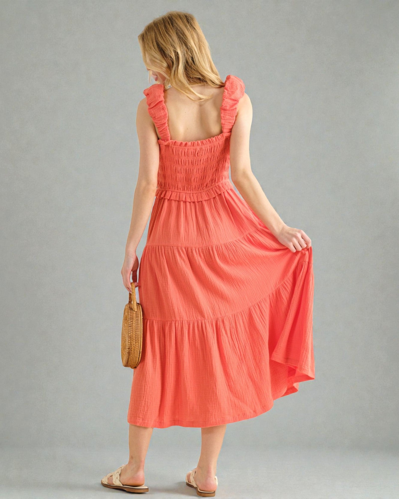 Woman wearing a coral dress holding a woven bag on a gray background