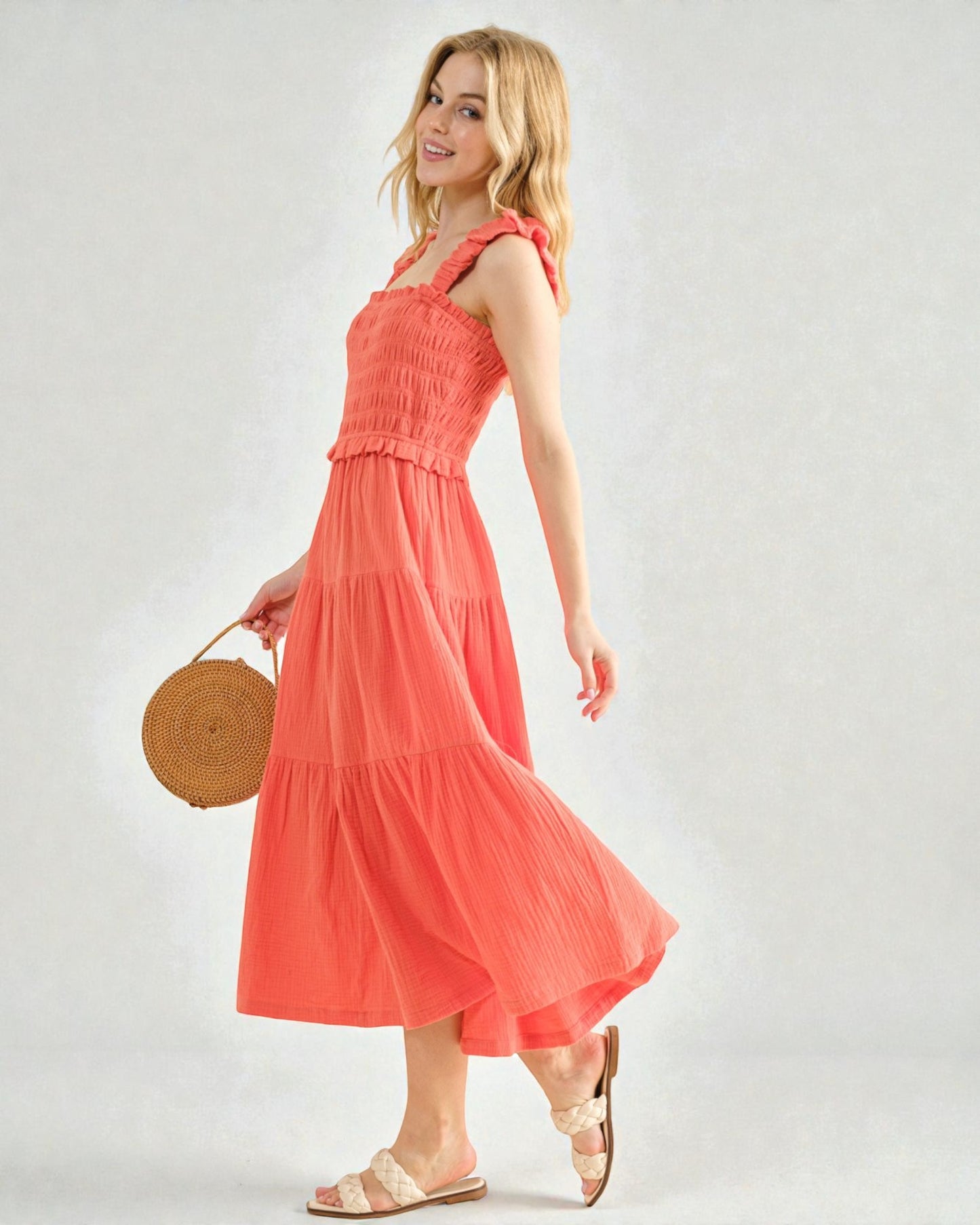 Woman wearing a coral dress holding a woven bag on a plain background