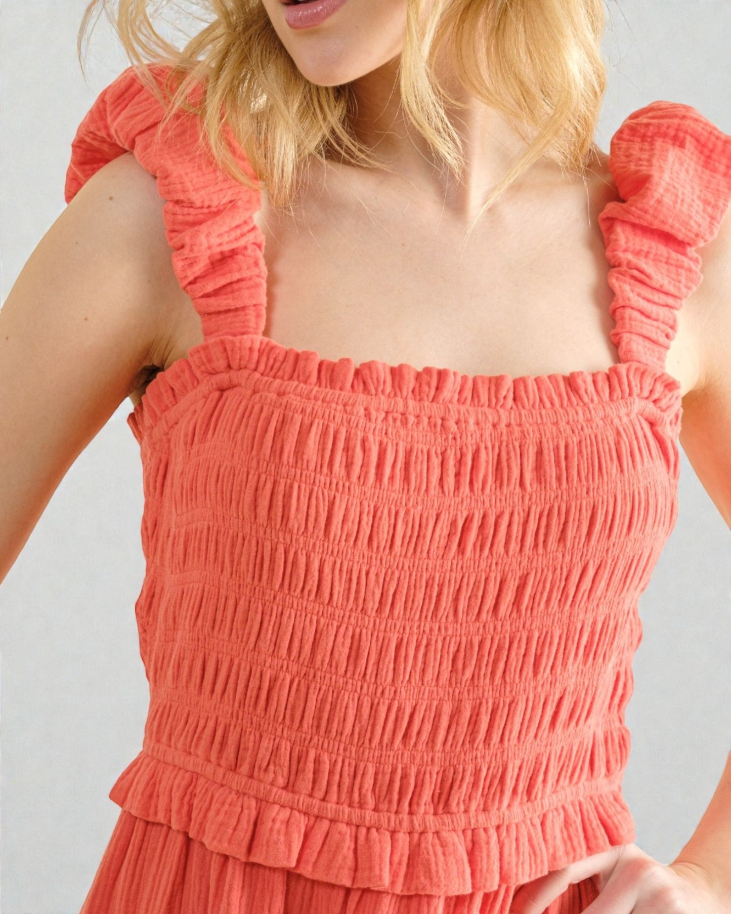 Coral smocked dress with ruffled straps on a plain background