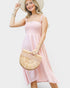 Woman in a pink dress holding a straw bag against a white background