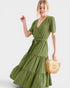 Woman wearing a green dress holding a woven bag on a white background