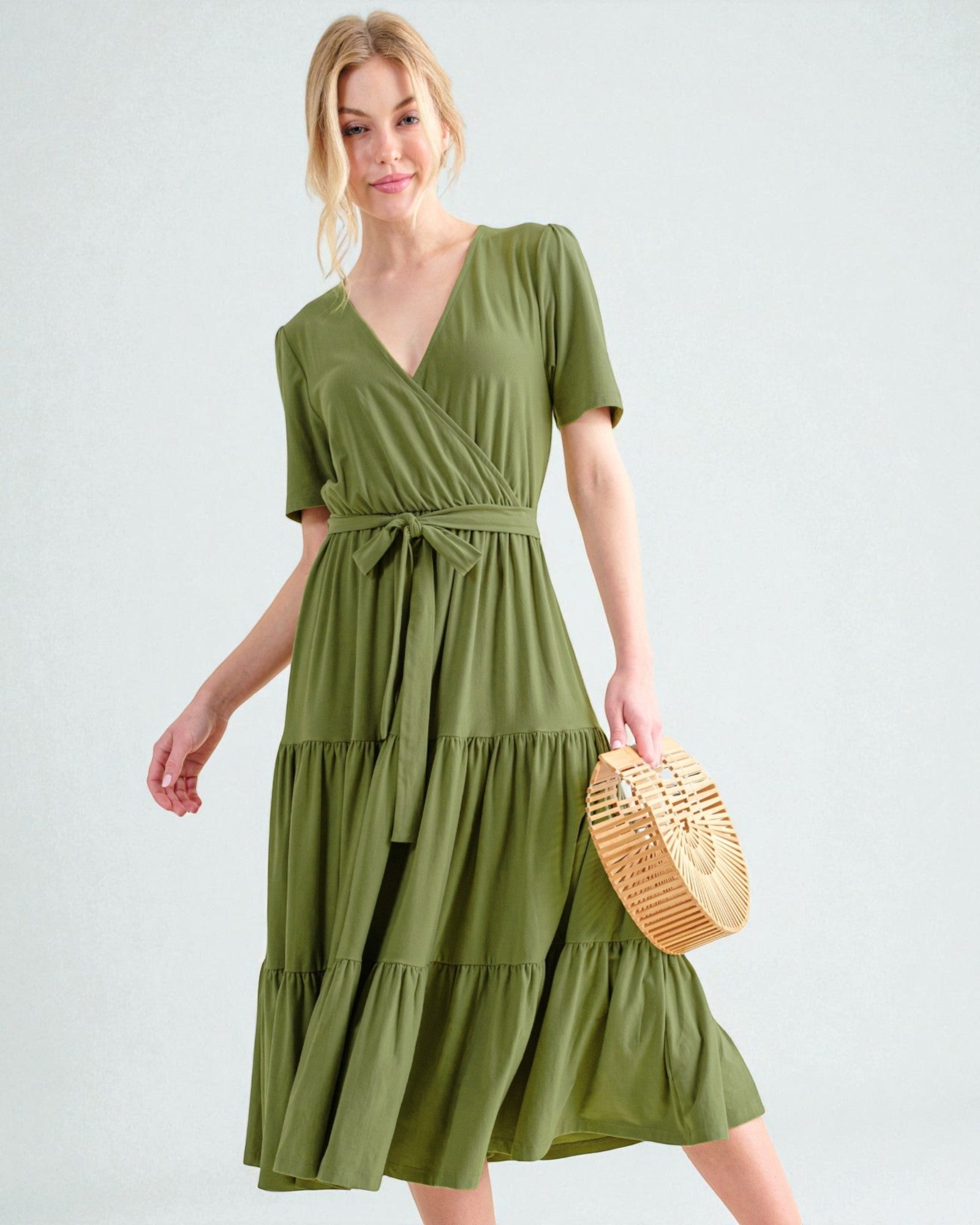 Woman wearing a green dress holding a woven bag on a light gray background