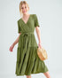 Woman wearing a green dress holding a woven bag on a light gray background