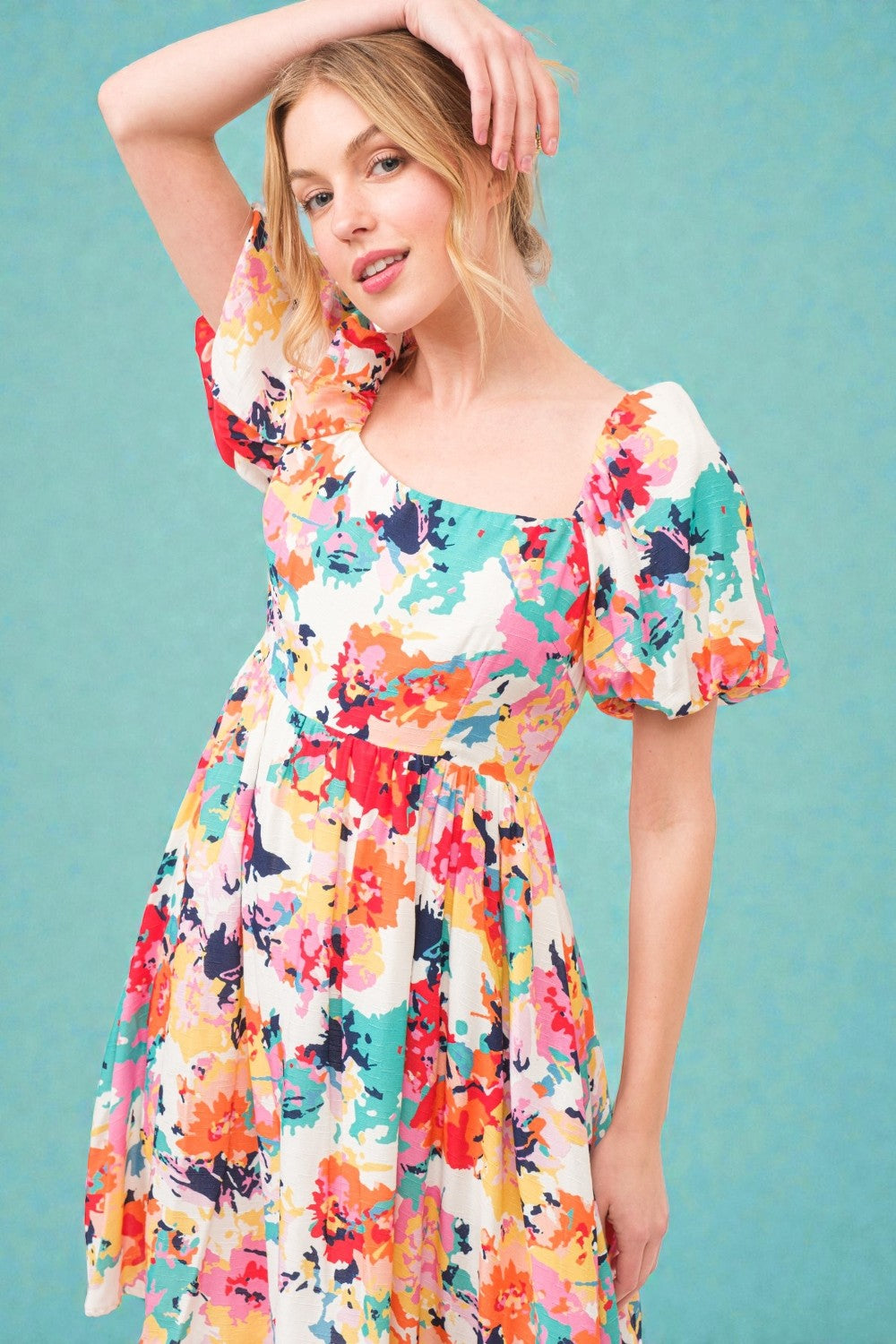 Woman wearing a colorful floral dress against a teal background