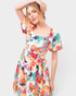 A woman modeling a short puff-sleeve dress with a colorful abstract floral print on a light background, set against a plain light gray studio backdrop.