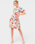A woman modeling a short puff-sleeve A-line dress with a vibrant multicolor floral print on a white base, set against a solid light gray background.
