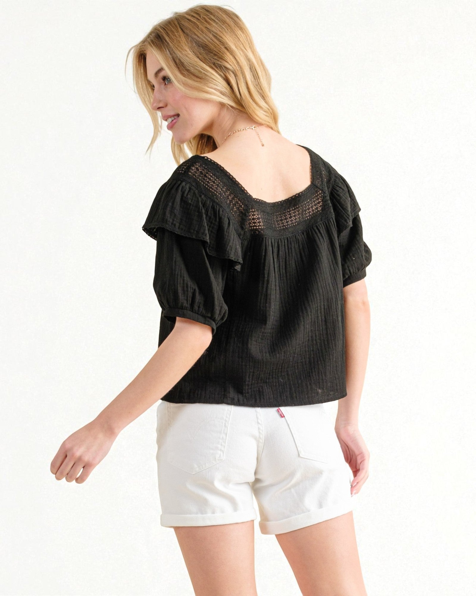 Woman wearing a black blouse with ruffled sleeves and white shorts on a white background
