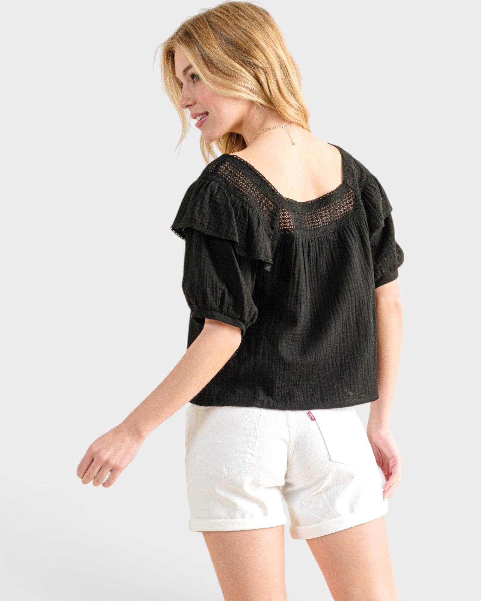 Woman wearing a black top and white shorts on a plain background