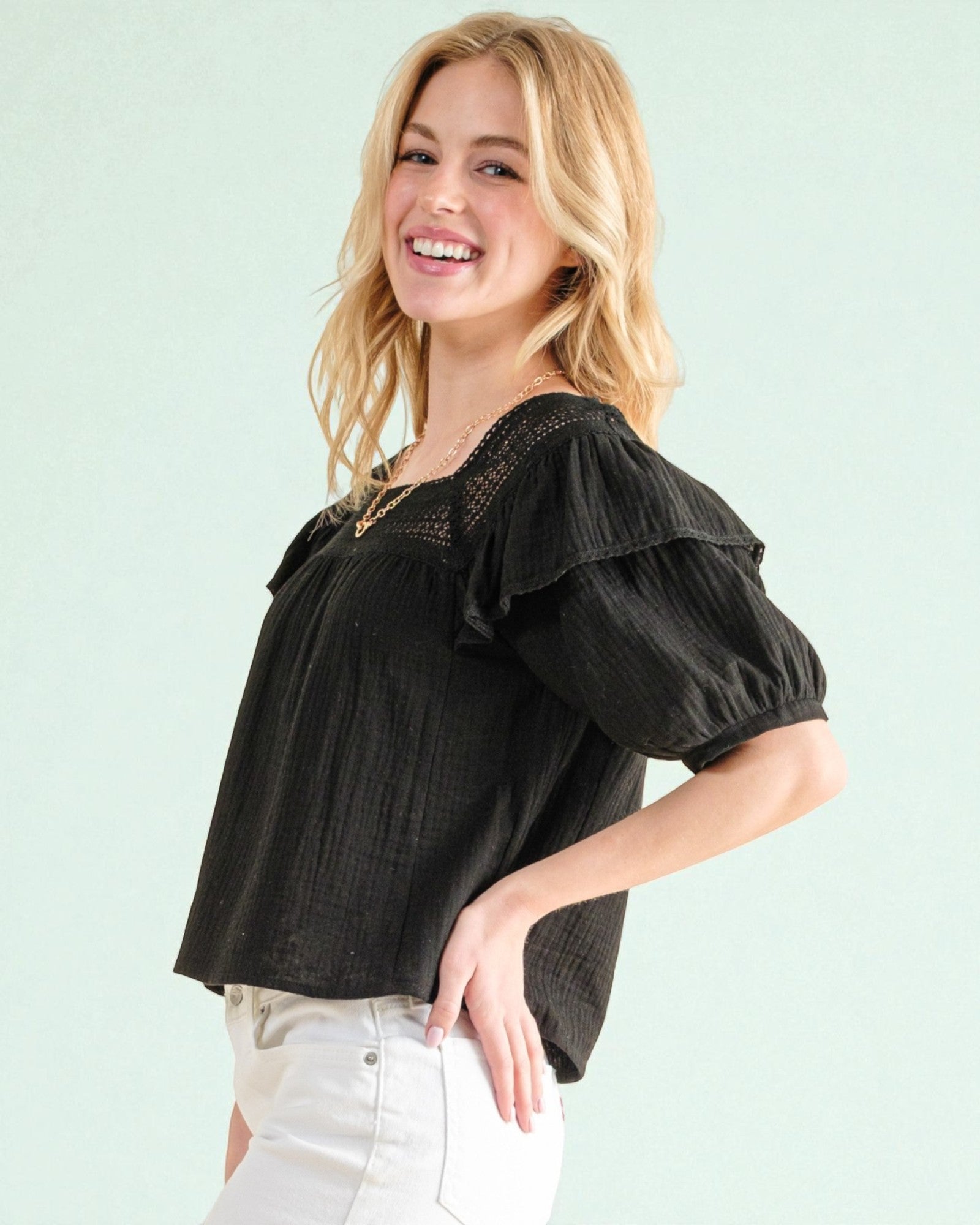 Woman wearing a black blouse with ruffled sleeves against a light green background