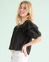 Woman wearing a black blouse with ruffled sleeves against a light green background