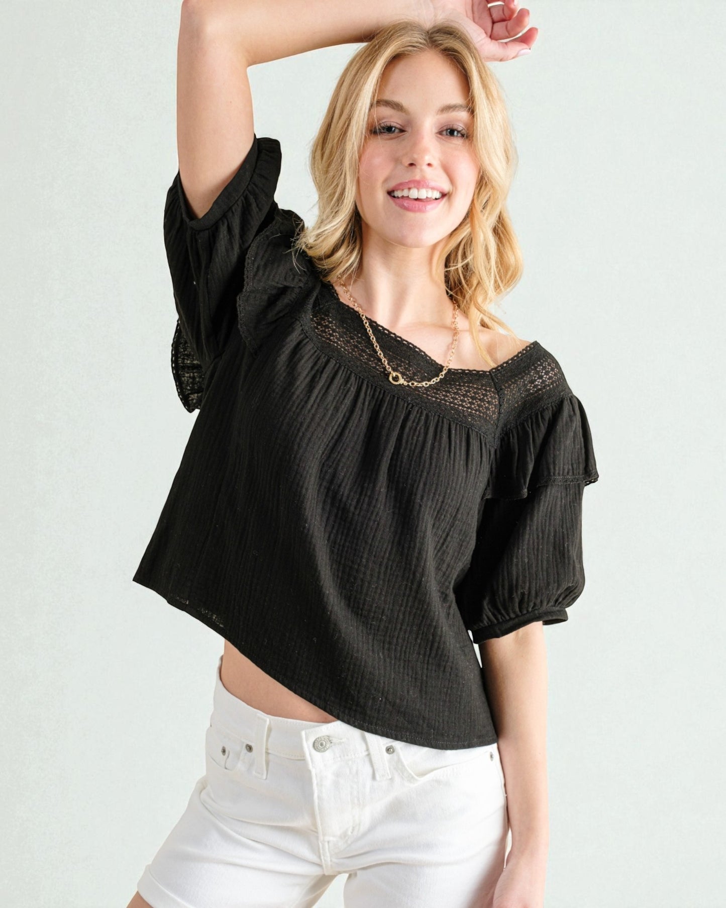 Woman wearing a black blouse with puffed sleeves and white pants on a plain background