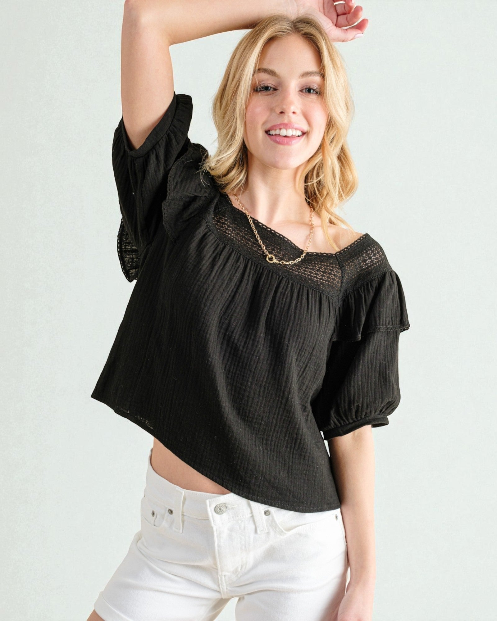 Woman wearing a black blouse with puffed sleeves and white pants on a plain background