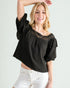 Woman wearing a black blouse with puffed sleeves and white pants on a plain background