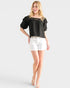 Woman wearing a black top and white shorts on a light gray background