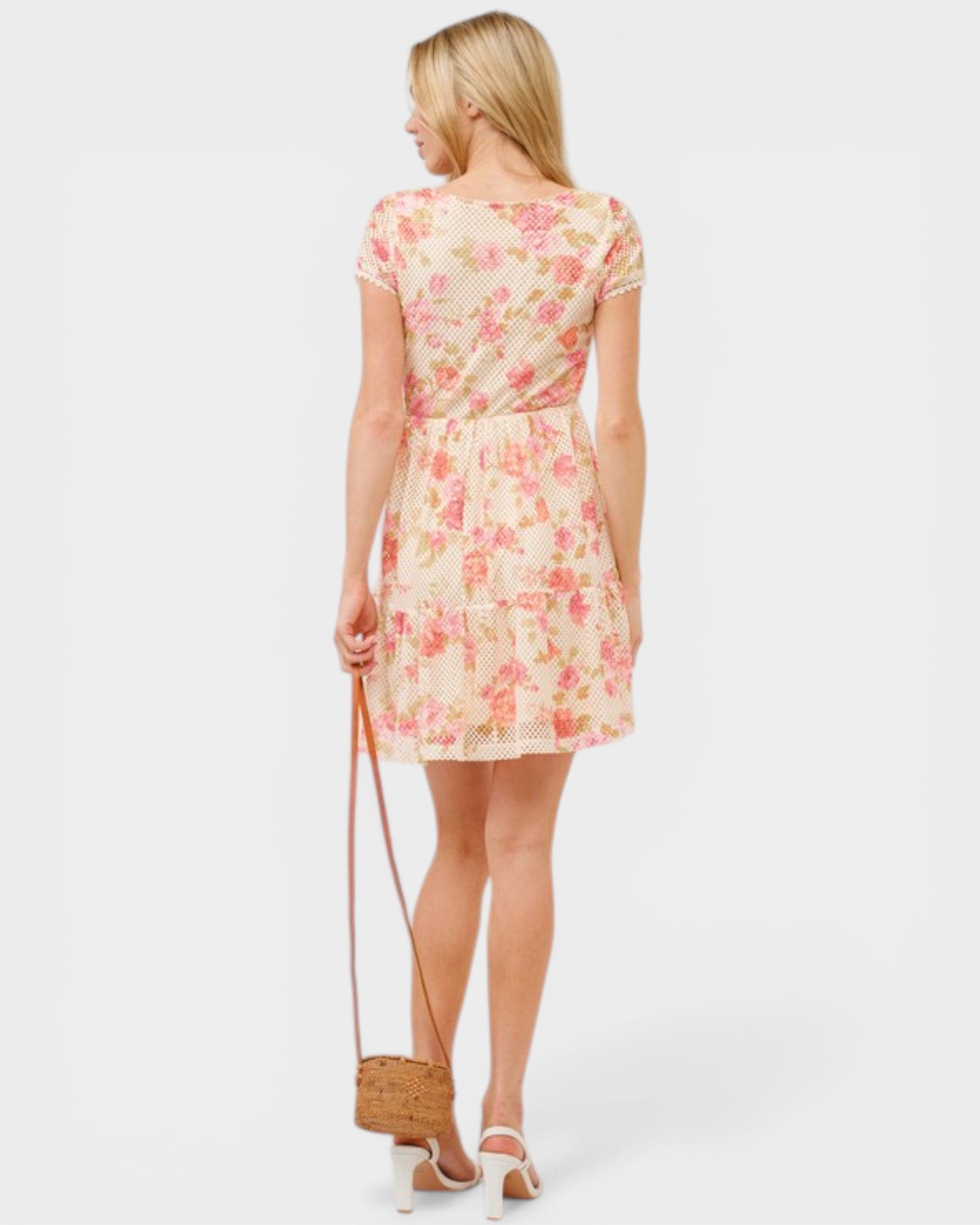 Woman wearing a floral dress holding a straw bag on a white background