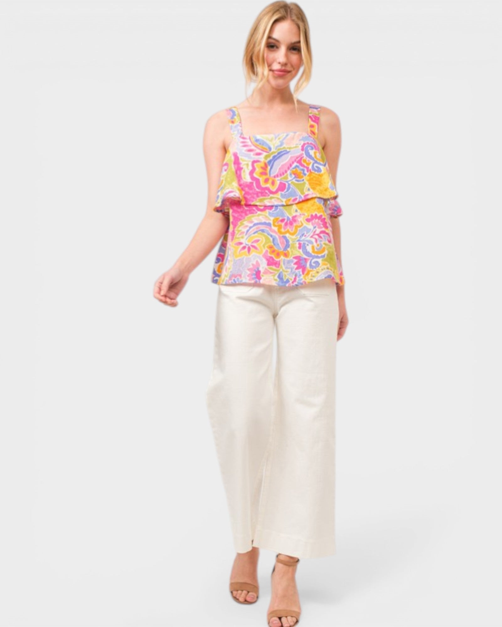 Woman wearing a colorful patterned top and white pants on a white background