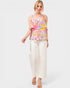 Woman wearing a colorful patterned top and white pants on a white background