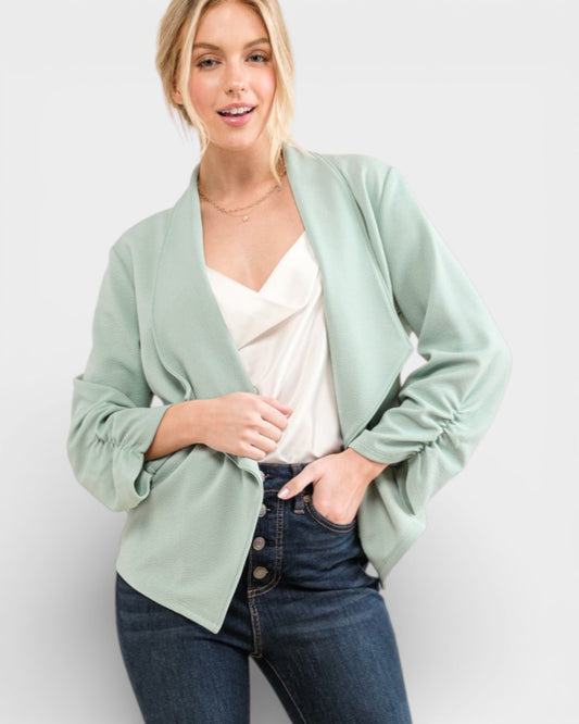 Woman wearing a light green blazer over a white top and blue jeans on a plain background